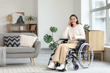 Young woman in wheelchair talking by mobile phone at home