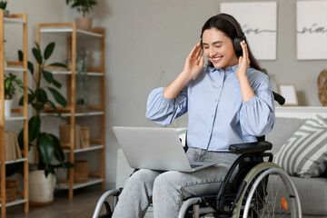 Young woman in wheelchair with headphones using laptop at home
