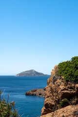 Vertical photo of a coast o a steep rocky cliff in  the Mediterranean sea at Attica-Greece. An island with blue sky at the background.
