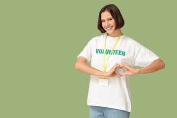 Young female volunteer making heart with her hands on green background