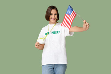 Young female volunteer with USA flag and blank badge on green background