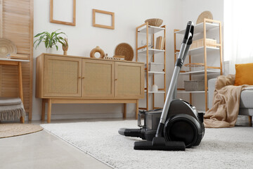 Interior of light living room with vacuum cleaner, drawers and shelf units