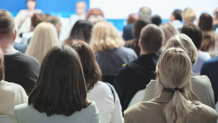 Obraz premium A large group of people are sitting in a room, some wearing glasses. Scene is one of focus and concentration, as the people are likely attending a lecture or presentation.