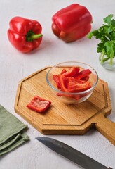 Sweet red pepper cut into squares in a glass bowl on a wooden board on a light concrete background. Ingredients for cooking.