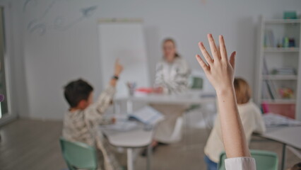 Obraz premium Unknown kids raising hands learning at school closeup. Blurred woman teacher
