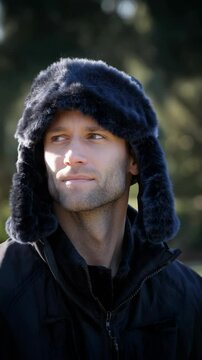 Portrait of a man in winter apparel featuring a fuzzy trapper hat and winter coat looking slightly off camera outdoors.