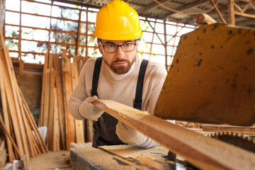 Male carpenter sawing wooden plank at sawmill