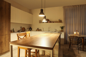 Interior of modern kitchen with tables, counters and glowing lamps in evening