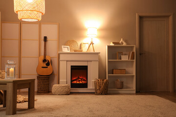 Interior of living room with fireplace, folding screen and glowing lamps in evening