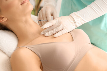 Young woman receiving injection in her neck on couch at cosmetologist's office, closeup