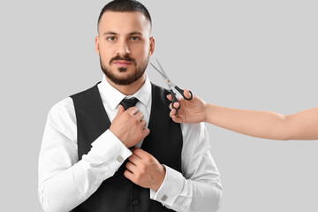 Handsome young bearded man and female hand with scissors on grey background