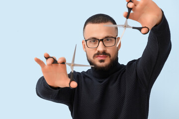 Handsome young bearded man with scissors on blue background