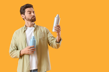 Thoughtful young man with bottles of laundry detergent on yellow background