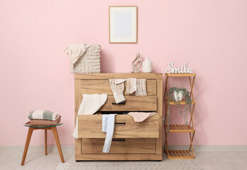 Obraz premium Shelving unit and commode with scattered clothes near pink wall in living room