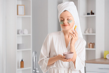Young woman with brush applying chia seeds face mask after shower in bathroom