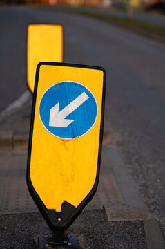 Keep left bollard with white on blue arrow on a yellow background on a suburban street in the United Kingdom. 