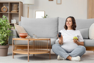 Young pregnant woman with glucometer and apple sitting at home. Gestational diabetes concept