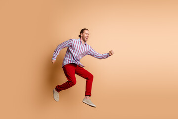 Fototapeta na wymiar Young man in casual striped shirt jumping with enthusiasm on beige background, expressing excitement and cheerful attitude