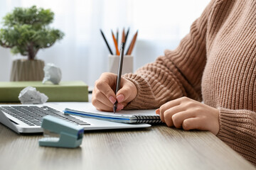 Woman writing on notebook at table in office, closeup