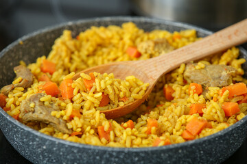 Frying pan with tasty pilaf and spatula in kitchen, closeup