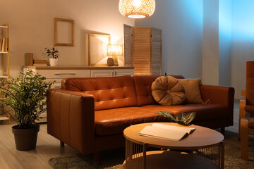 Interior of living room with brown sofa, table and glowing lamps in evening