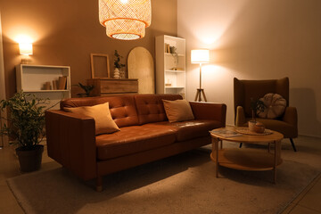 Interior of living room with brown sofa, armchair and glowing lamps in evening