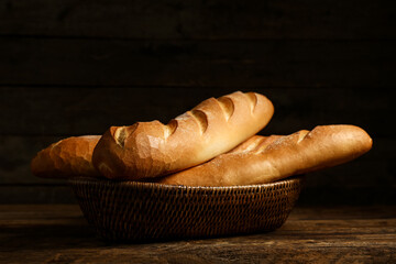Wicker bowl with fresh baguettes on wooden background