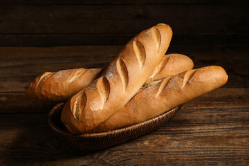 Wicker bowl with fresh baguettes on wooden background