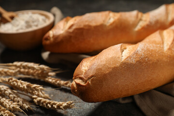 Fresh baguettes with wheat and wooden bowl of flour on dark background, closeup