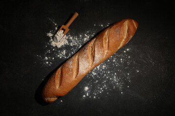 Fresh baguette and wooden scoop with flour on black background
