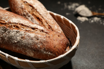 Wicker basket with fresh rye baguettes on black background, closeup