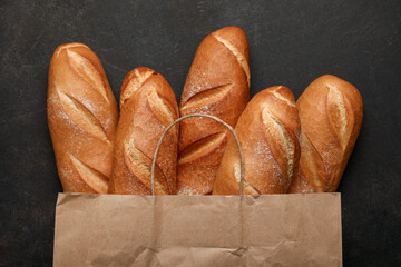 Paper bag with fresh baguettes on black background
