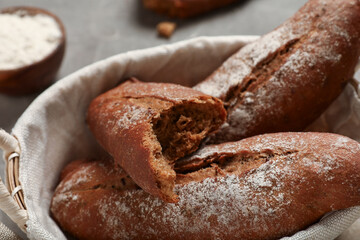 Wicker basket with fresh rye baguettes on grey background, closeup