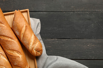 Tray with fresh baguettes on black wooden background
