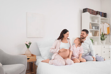 Cute little girl with her pregnant mother and father sitting in bedroom