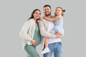 Cute little girl with her pregnant mother and father on light background