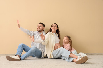 Cute little girl with her pregnant mother and father sitting near beige wall