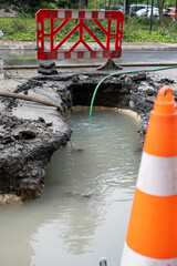 Flooded Road Construction Site with Water Pipe
A muddy construction site with standing water in a trench, featuring a green hose and an orange traffic cone in the foreground.
