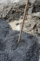 Shovel in gravel pile at construction site
Close-up of a shovel stuck into a mound of dark gravel, surrounded by crushed rock and soil at a roadwork location.
