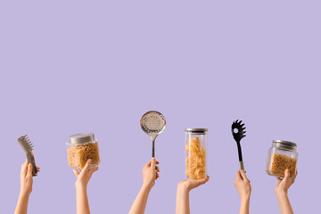 Female hands with kitchen utensils and jars of pasta on lilac background