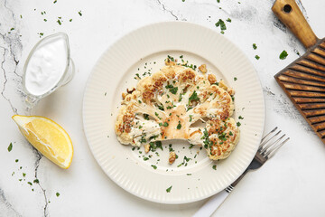 Plate with grilled cauliflower steak, lemon and gravy boat of sauce on white background