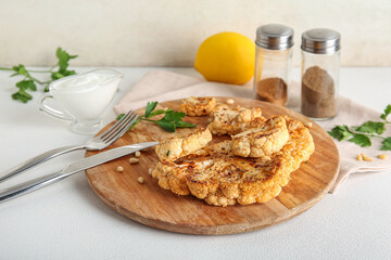 Wooden board of grilled cauliflower steaks with parsley and nuts on white background