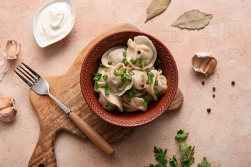 Bowl of delicious boiled dumplings with green onion and sour cream on beige background