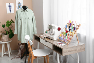 Tailor's workplace with sewing machine and thread spools near window in atelier