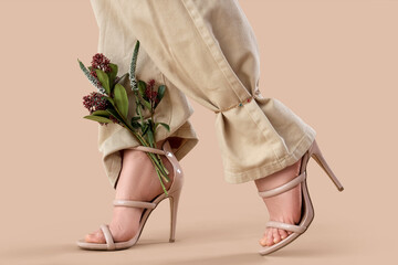 Legs of young woman in stylish high heels with beautiful flowers on brown background