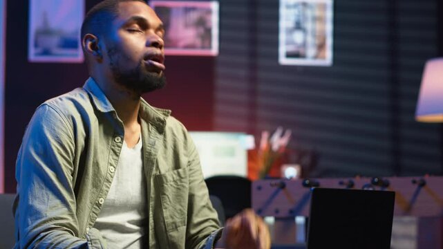 African american person receiving some bad news while doing remote work tasks, feeling overworked and under pressure to complete all his assignments. Young adult deals with burnout. Camera B.