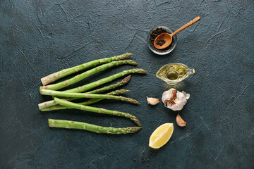 Fresh green asparagus with lemon, garlic, peppercorns and gravy boat of oil on dark background