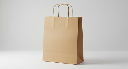 A simple brown paper shopping bag with handles standing on a white surface in studio lighting