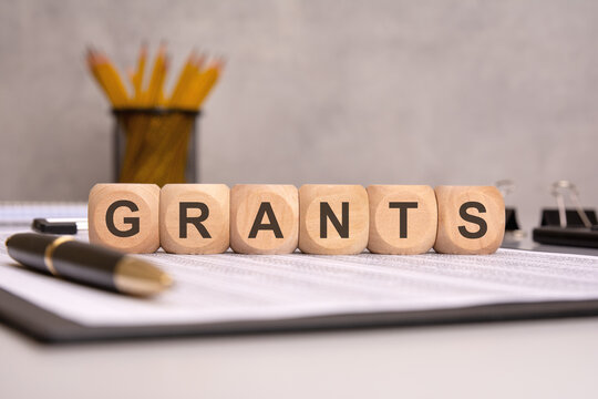 Word GRANTS on wooden blocks with office supplies in background.