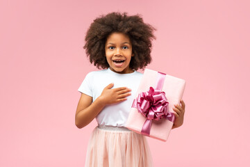 Studio portrait of cute joyful African American girl holding decorated gift box and pressing hand...